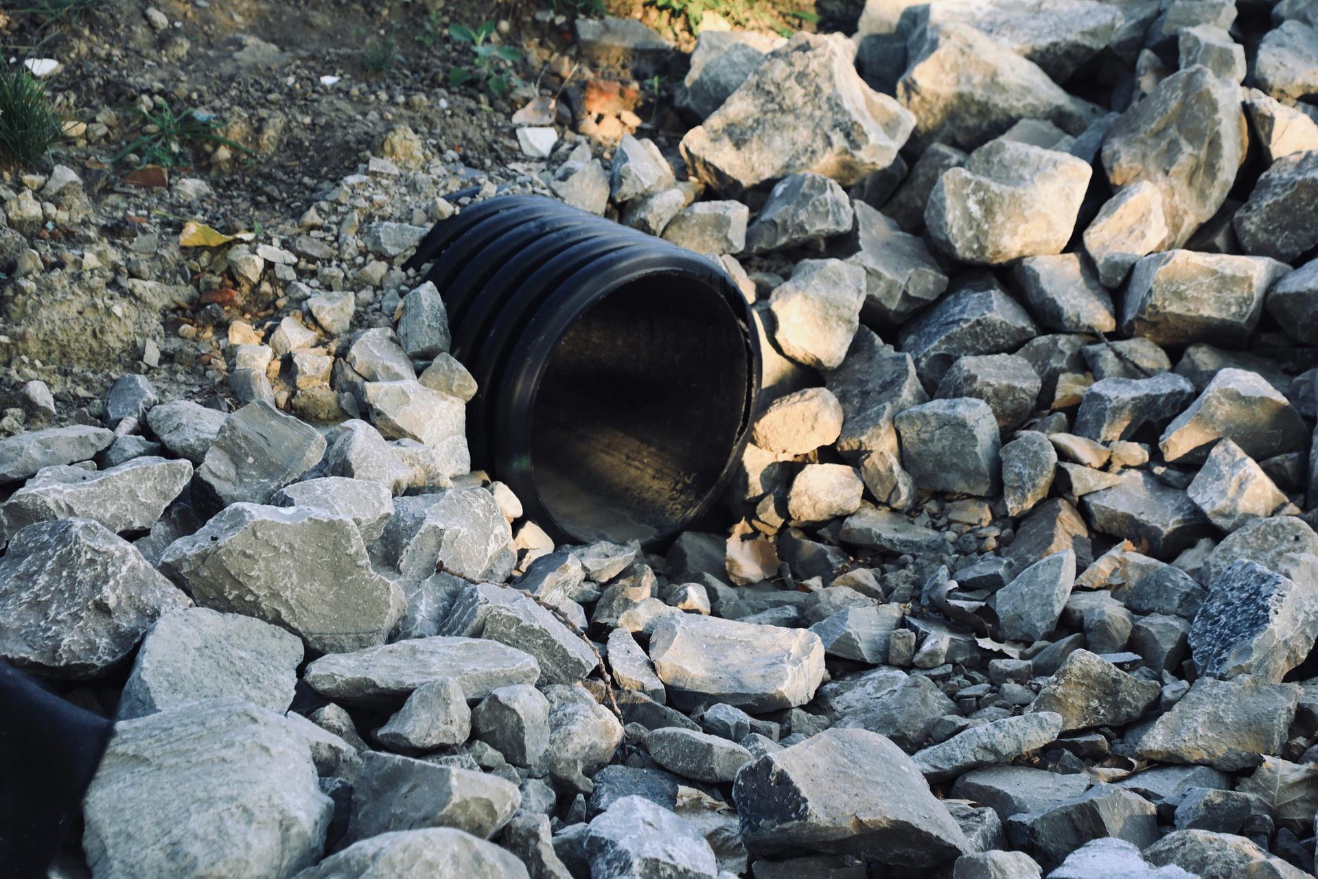 A Black Pipe On Top Of A Pile Of Rocks — Hawthorne, NY — Better Home Sewage Services, Inc.