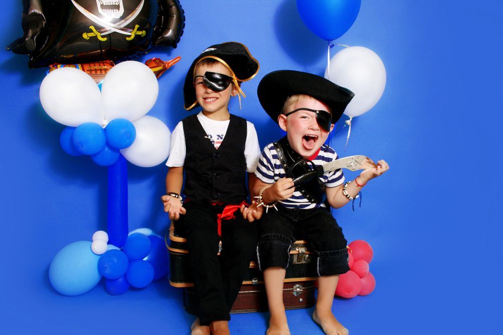 Due bambini in costume da pirata posano con dei palloncini su uno sfondo blu.