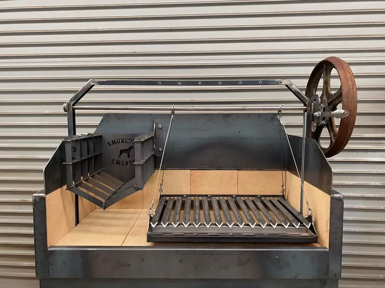 A metal grill with a wheel attached to it is sitting in front of a metal wall.