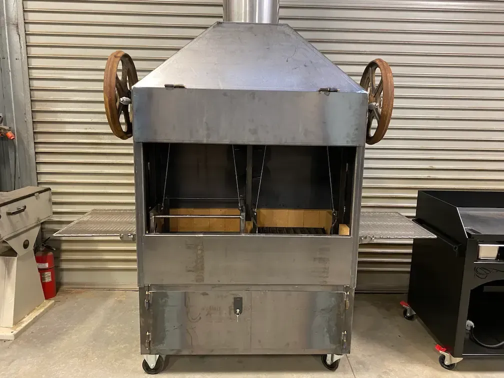 A large stainless steel grill with wheels is sitting in front of a garage door.