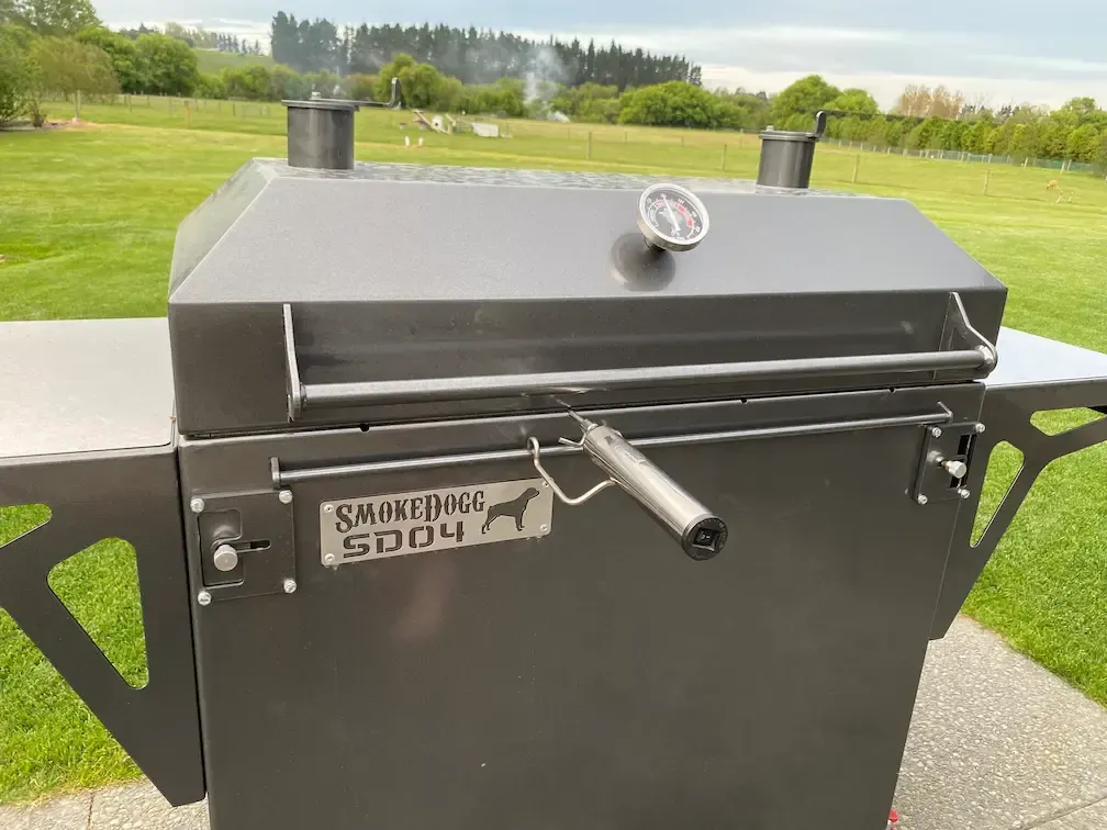 A black grill is sitting on a sidewalk in front of a grassy field.