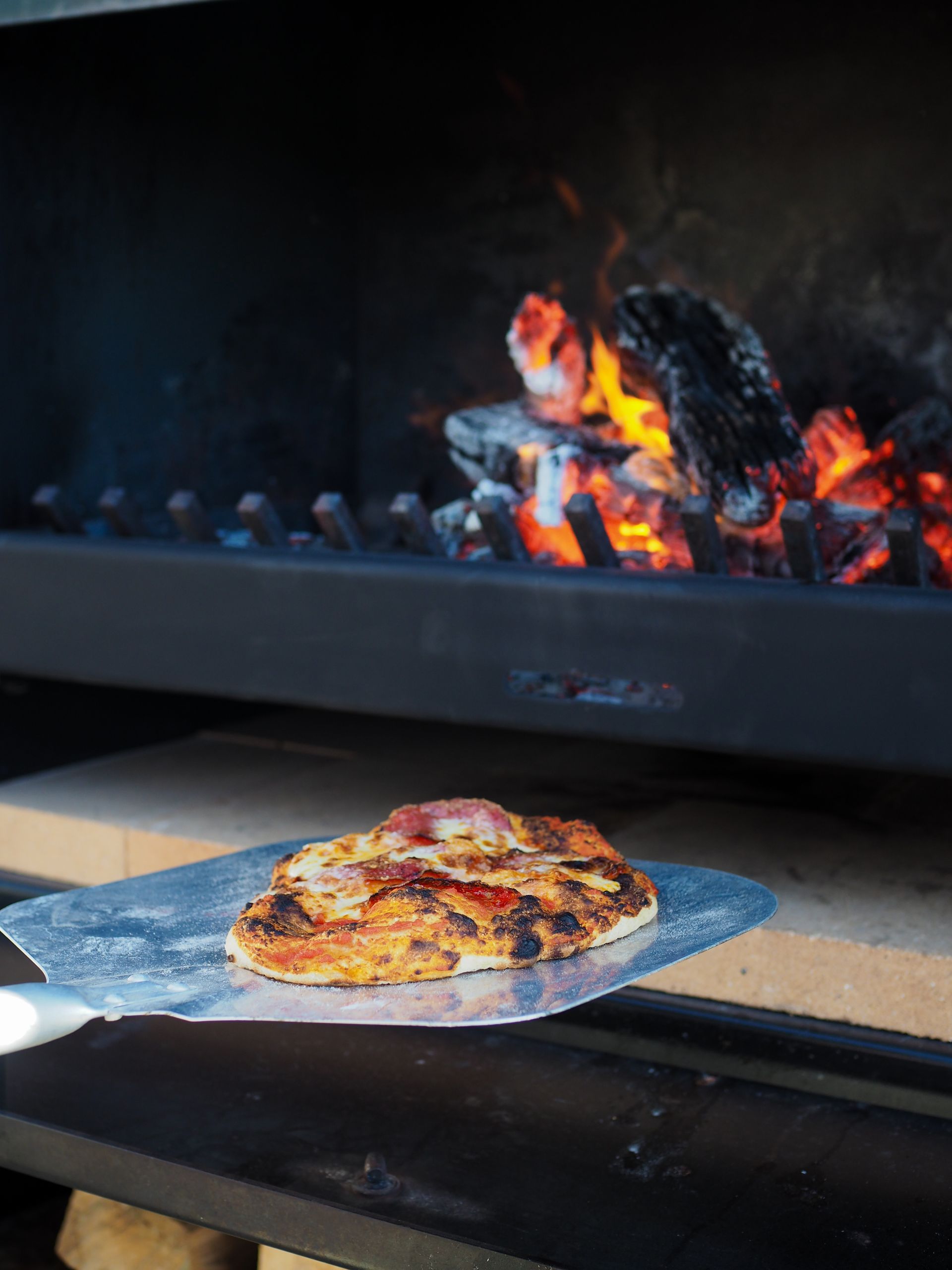 A pizza is being cooked in an outdoor oven
