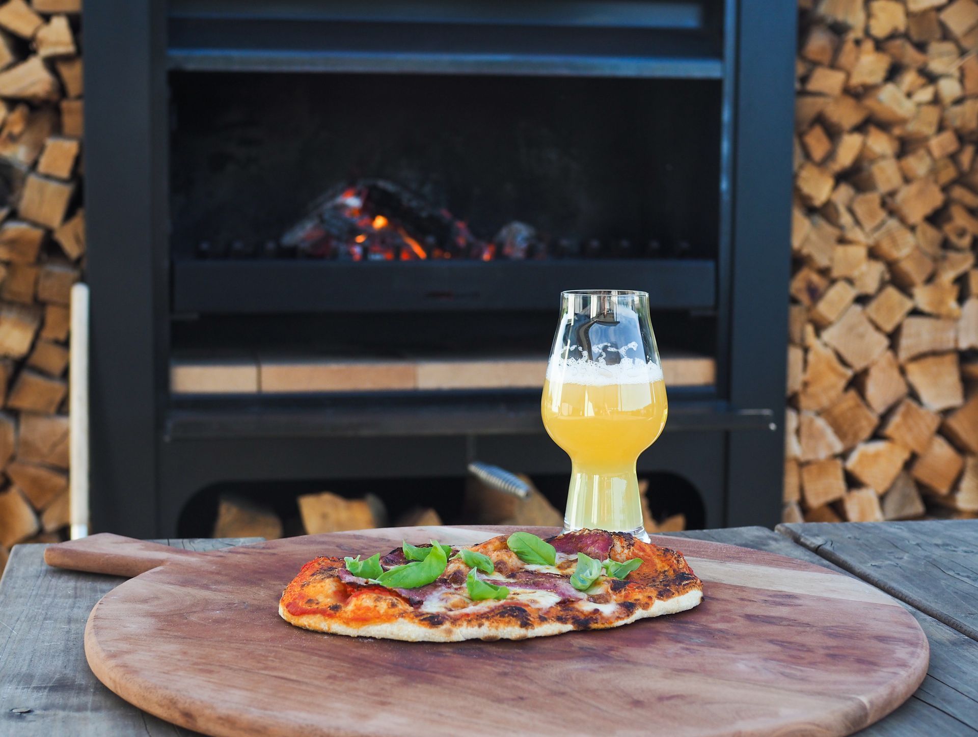 A pizza is sitting on a wooden cutting board next to a glass of beer.