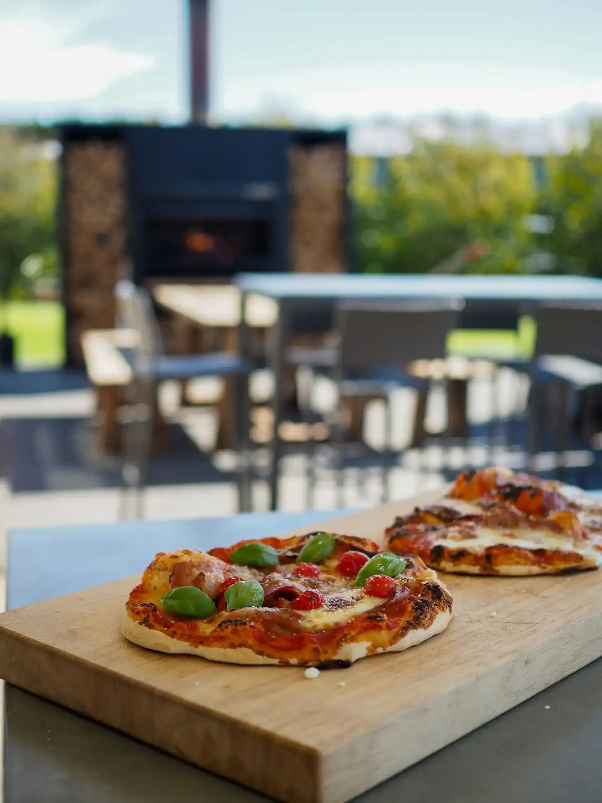 Two pizzas are sitting on a wooden cutting board.