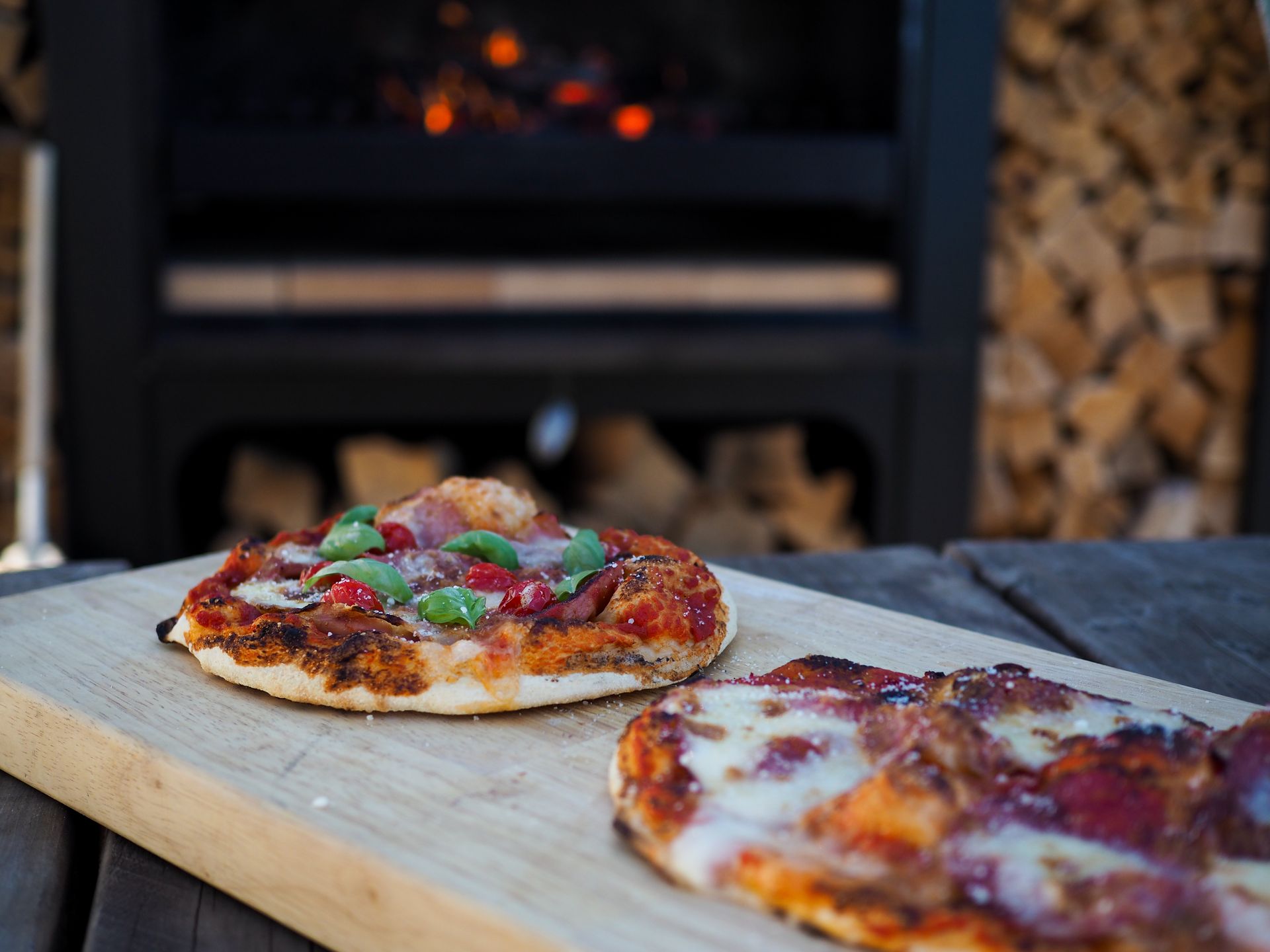 Two pizzas are sitting on a wooden cutting board in front of a fireplace.