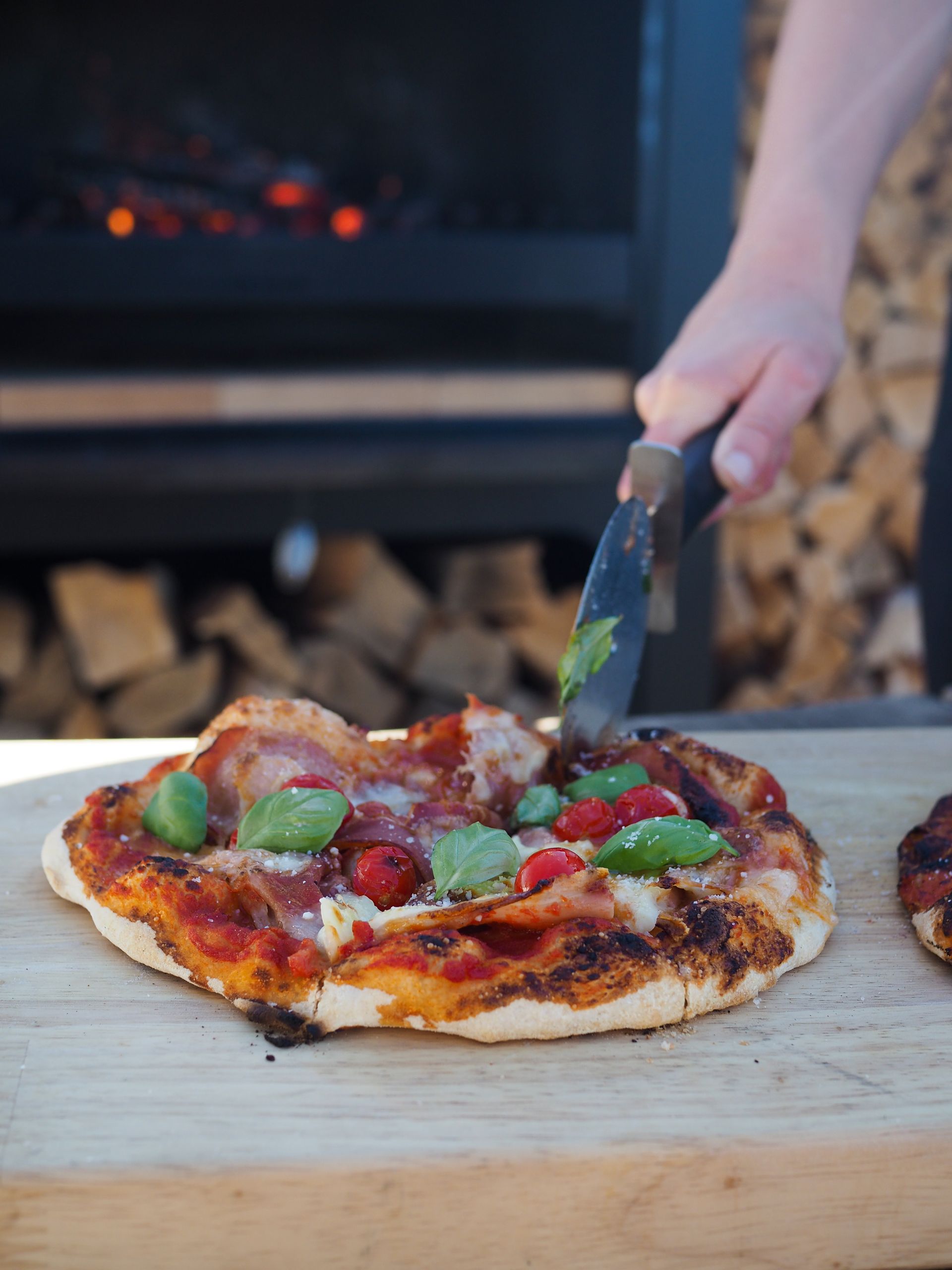 A person is cutting a pizza on a wooden cutting board