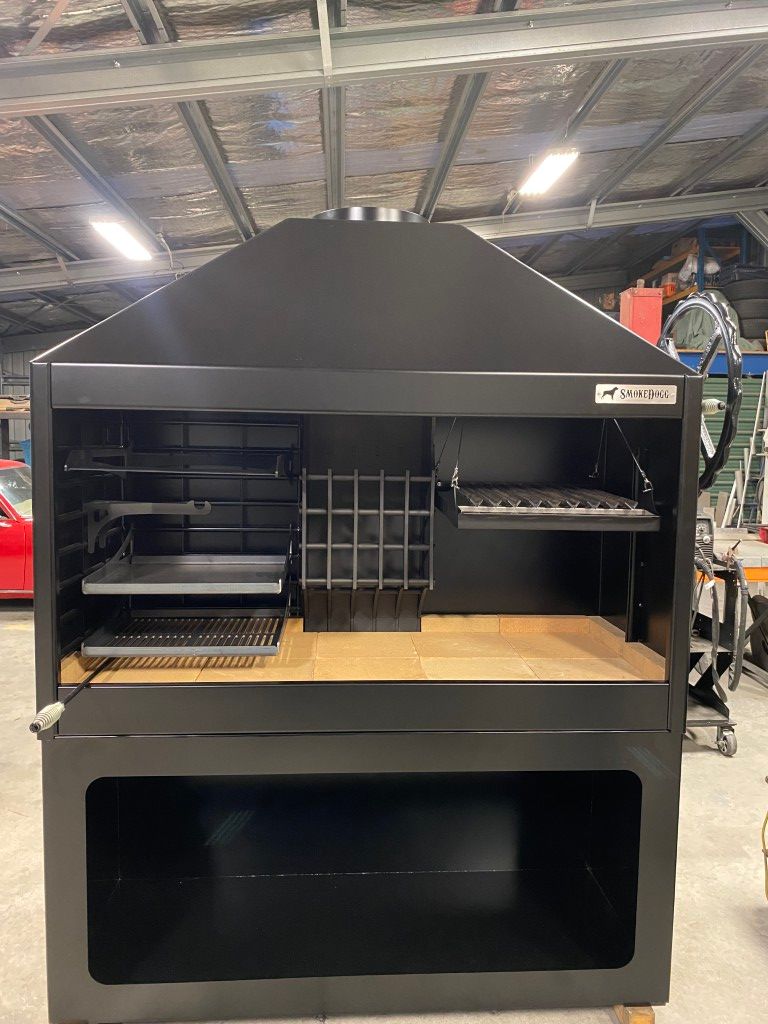 A large black grill with a hood is sitting in a warehouse.