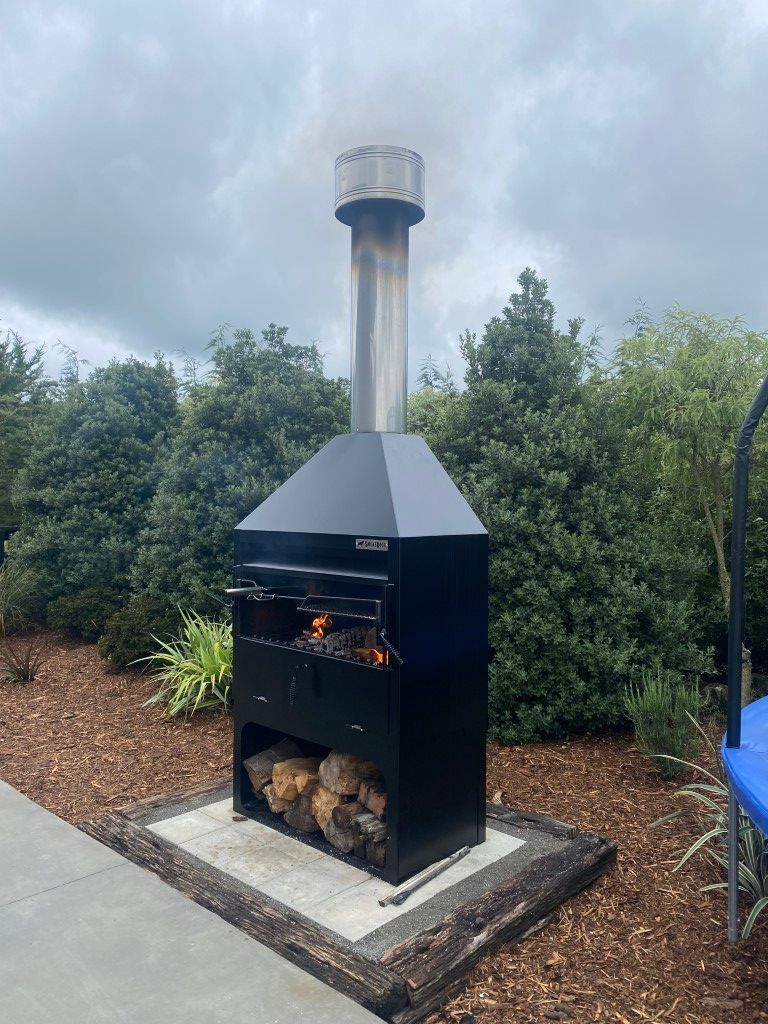 A black grill with a chimney on top of it is sitting on top of a concrete patio.