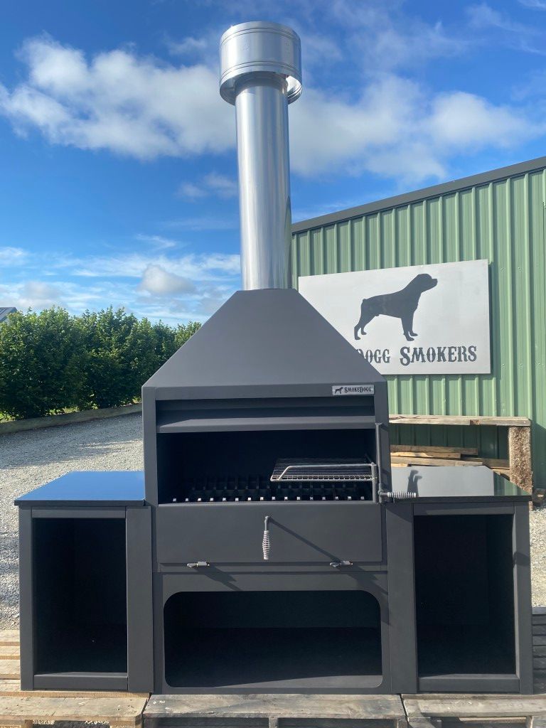 A large grill is sitting in front of a sign that says smokehs