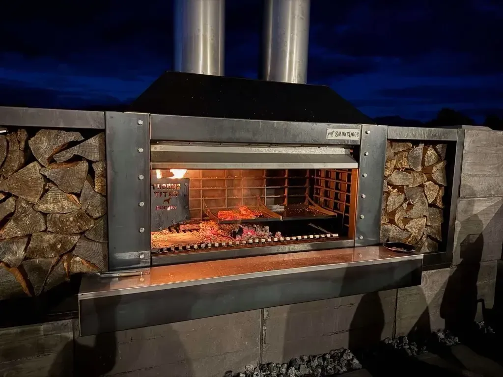 A grill is built into a wall next to a pile of wood.