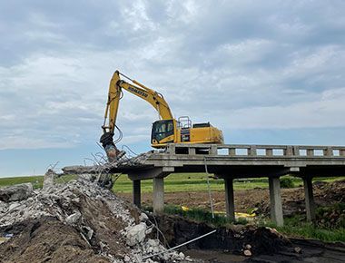 A large yellow excavator is demolishing a bridge.