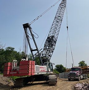 A large crane is sitting on top of a dirt road next to a truck.