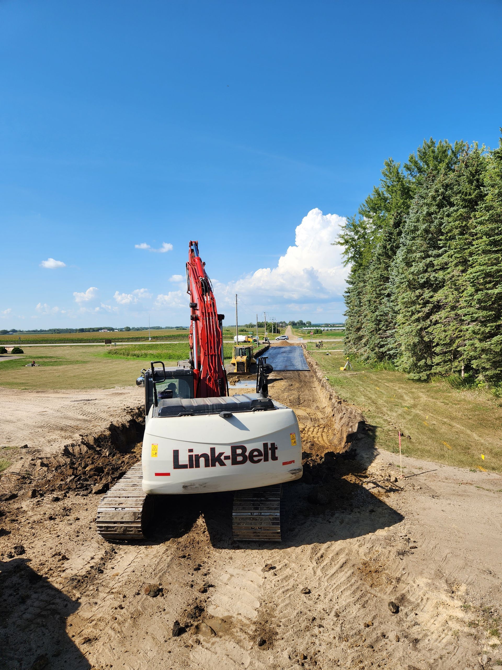 Link-Belt excavator digging a trench in a field on a sunny day.