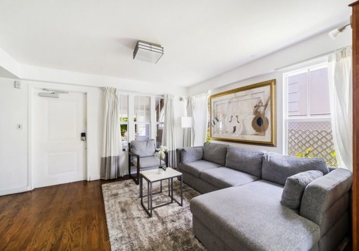 Bright living room with gray sectional sofa, coffee table, wall art, wood floor, and white walls.