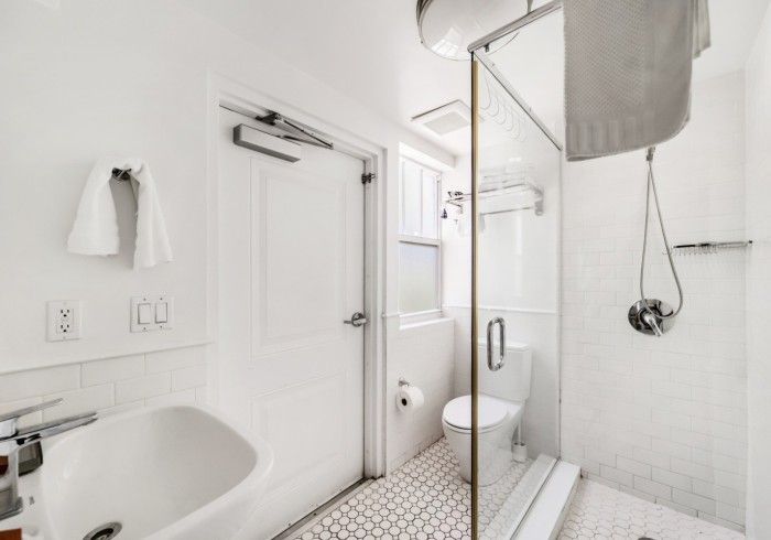 Bright white bathroom with sink, toilet, tiled floor, and glass shower enclosure.