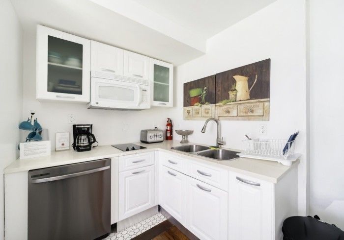 White corner kitchen with cabinets, stainless dishwasher, microwave, coffee maker, and sink beneath wall art
