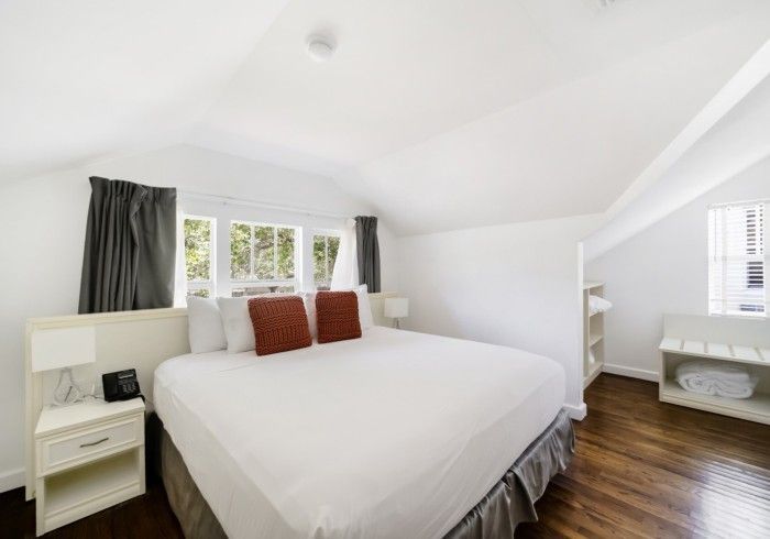 Bright white bedroom with a large bed, bedside table, windows, and dark wood floor