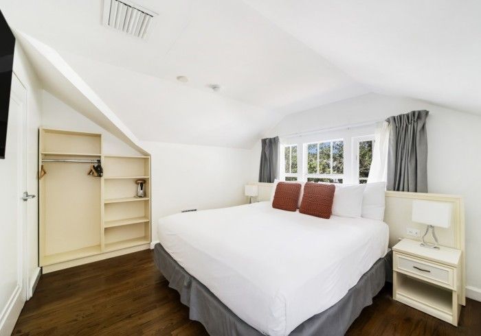 Bright bedroom with a white bed, gray curtains, built-in closet, and dark wood floor