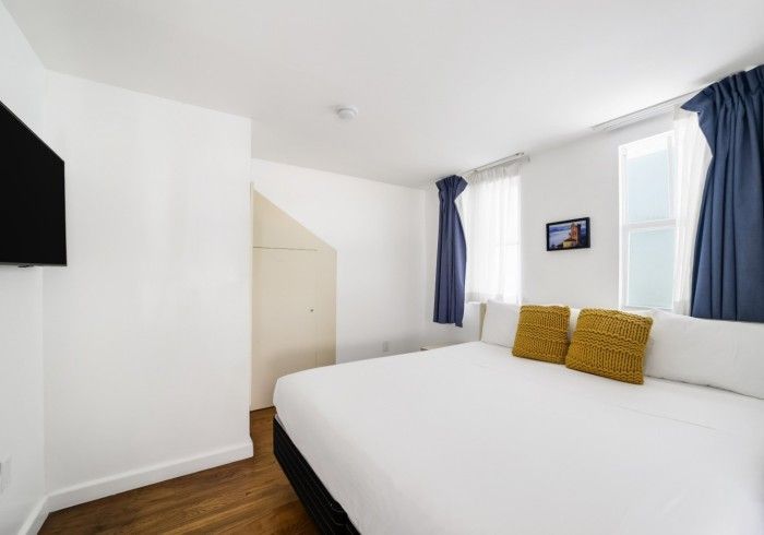 Bright white bedroom with a large bed, blue curtains, and a small wall-mounted TV.