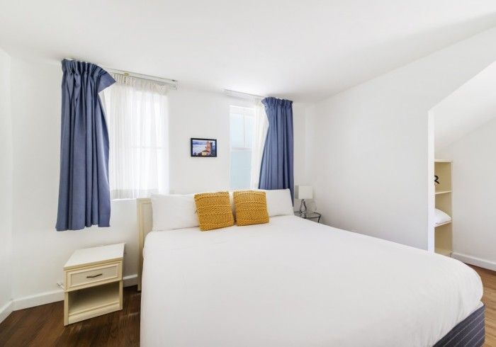 Bright white bedroom with blue curtains, a neatly made bed, and small bedside tables.