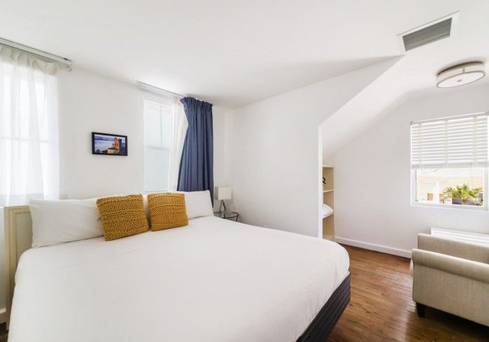 Bright bedroom with white bed, mustard pillows, wood floor, and soft natural light