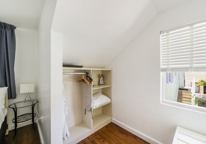 Small empty bedroom corner with open closet, window blinds, white walls, and hardwood floor