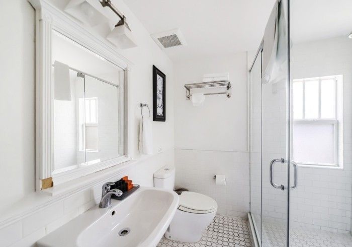 Bright white bathroom with a sink, toilet, shower, mirror, and small window.