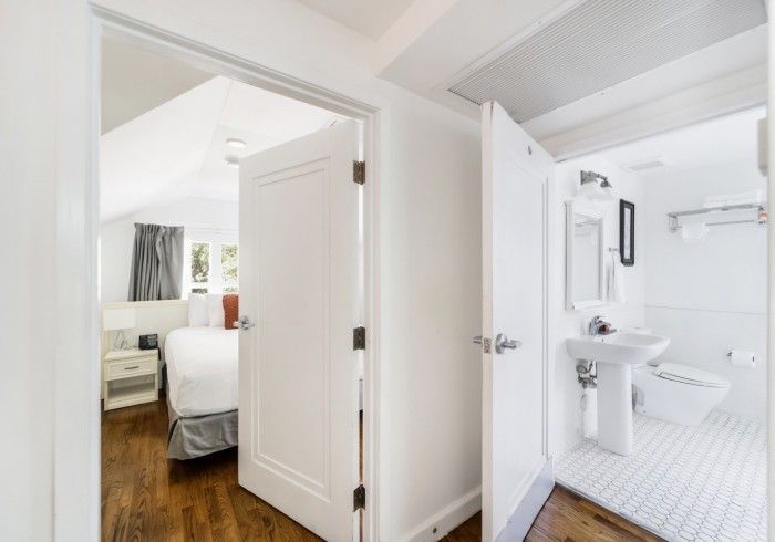 Bright hallway with open doors showing a bedroom and a white bathroom with patterned floor tiles.