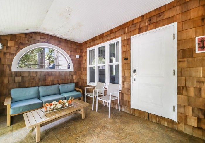 Bright sunroom with teal sofa, coffee table, white chair, arched window, and white door on wood-paneled walls