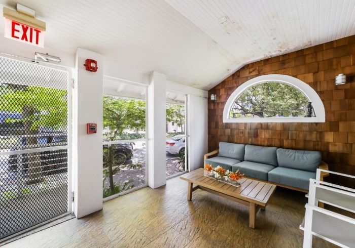 Cozy lobby seating area with gray sofa, wooden coffee table, arched window, and glass door entrance