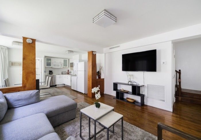 Modern living room with gray sofa, wall-mounted TV, wood floors, and open kitchen area