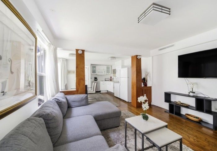 Bright living room with gray sectional sofa, wall TV, coffee table, and open kitchen in the background