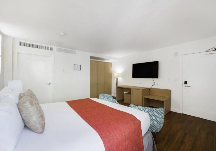 Bright bedroom with bed, red runner, desk, wall-mounted TV, and white doors.