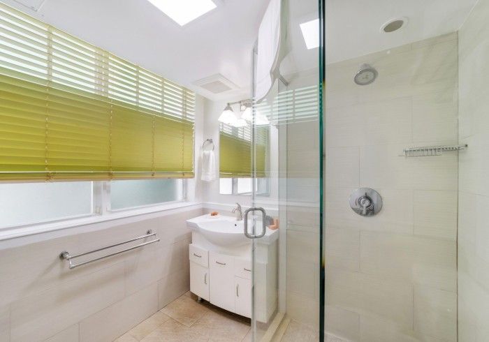 Bright modern bathroom with green blinds, white vanity, large mirror, and glass shower