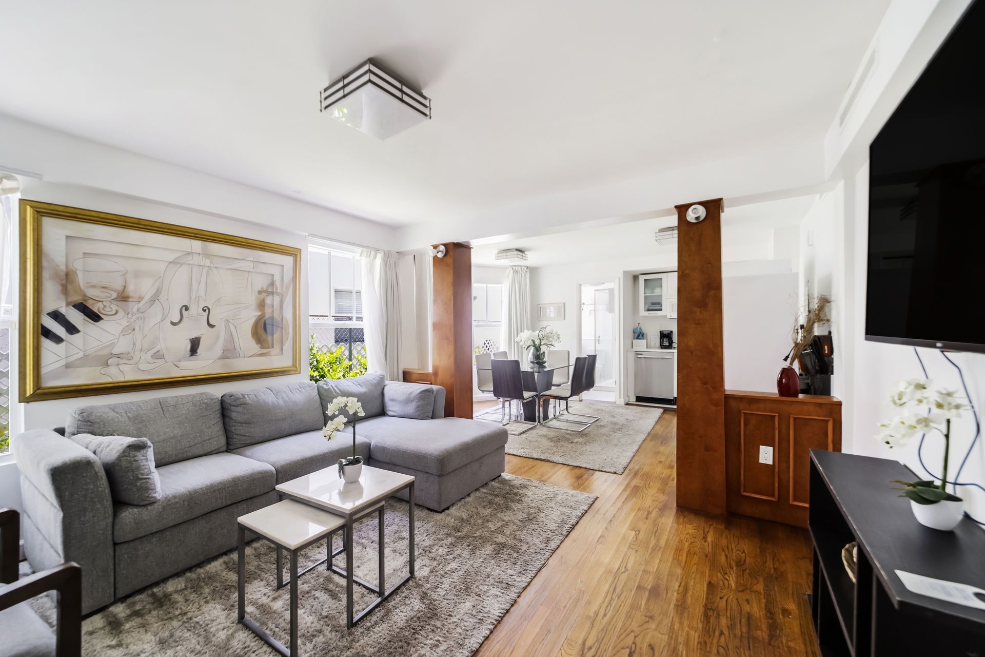 Bright living room with gray sofa, coffee tables, wood floors, and dining area beyond
