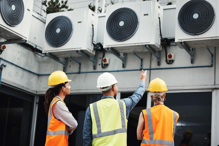 A group of construction workers are standing in front of a building looking at air conditioners.