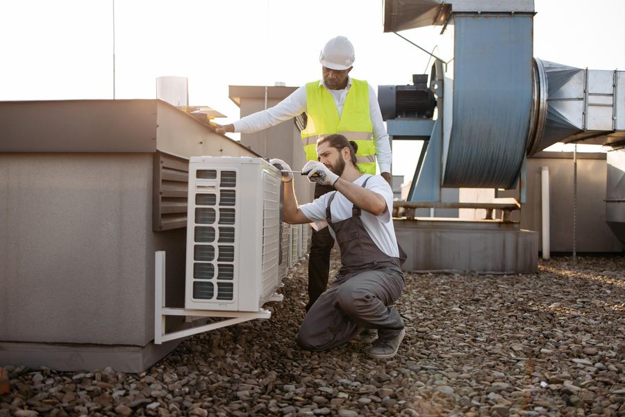 Two men are working on an air conditioner on the roof of a building.