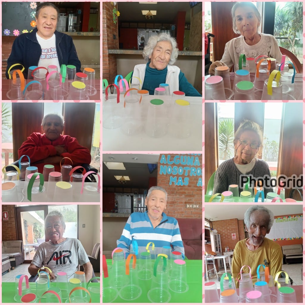 Personas mayores en un centro juegan a un juego de vasos con accesorios coloridos. Sonríen, mostrando una divertida actividad en interiores.