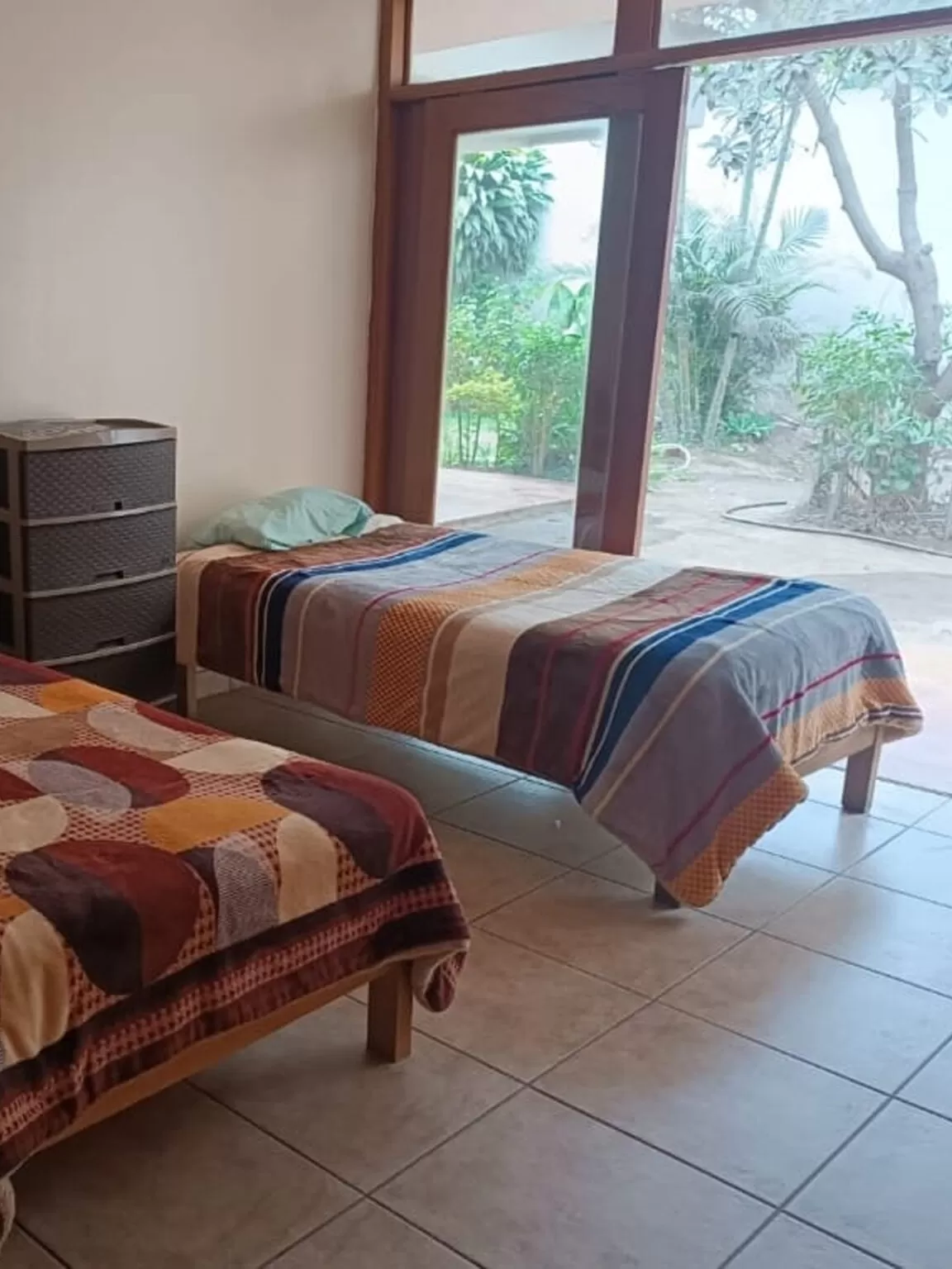 Dos camas con mantas estampadas en una habitación. Una cómoda junto a una ventana con vista al exterior.