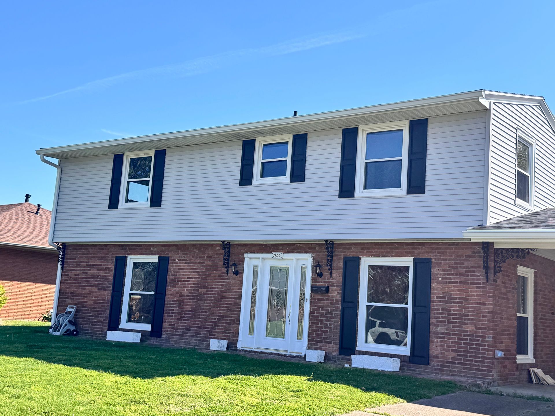 Two-story brick-and-white suburban house with black shutters under a clear blue sky