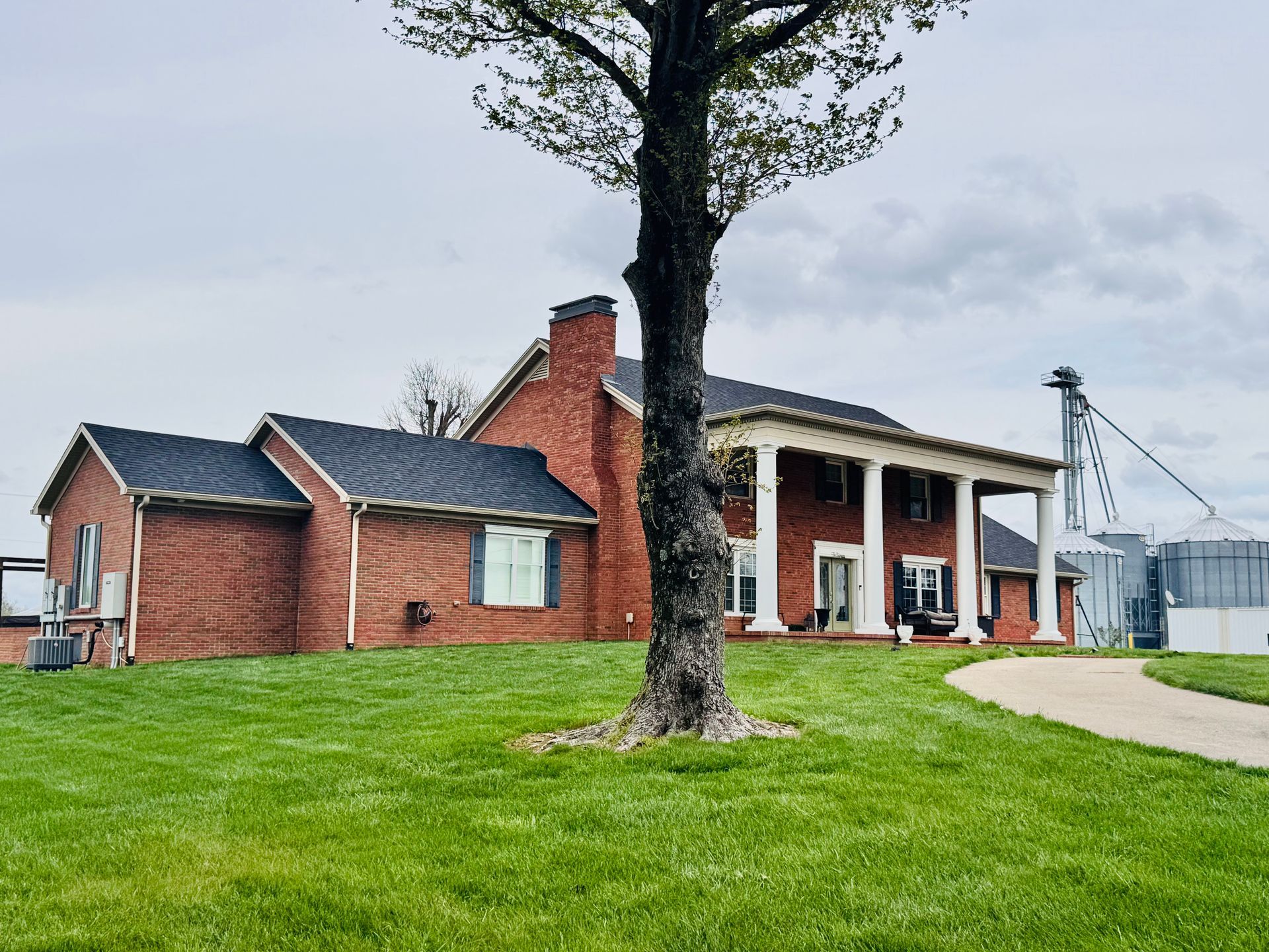 Red brick building with white porch columns beside a large tree and green lawn