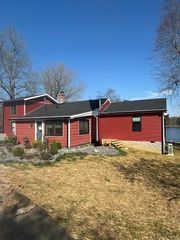 Red house with black roof and porch in a leaf-covered yard under a clear blue sky
