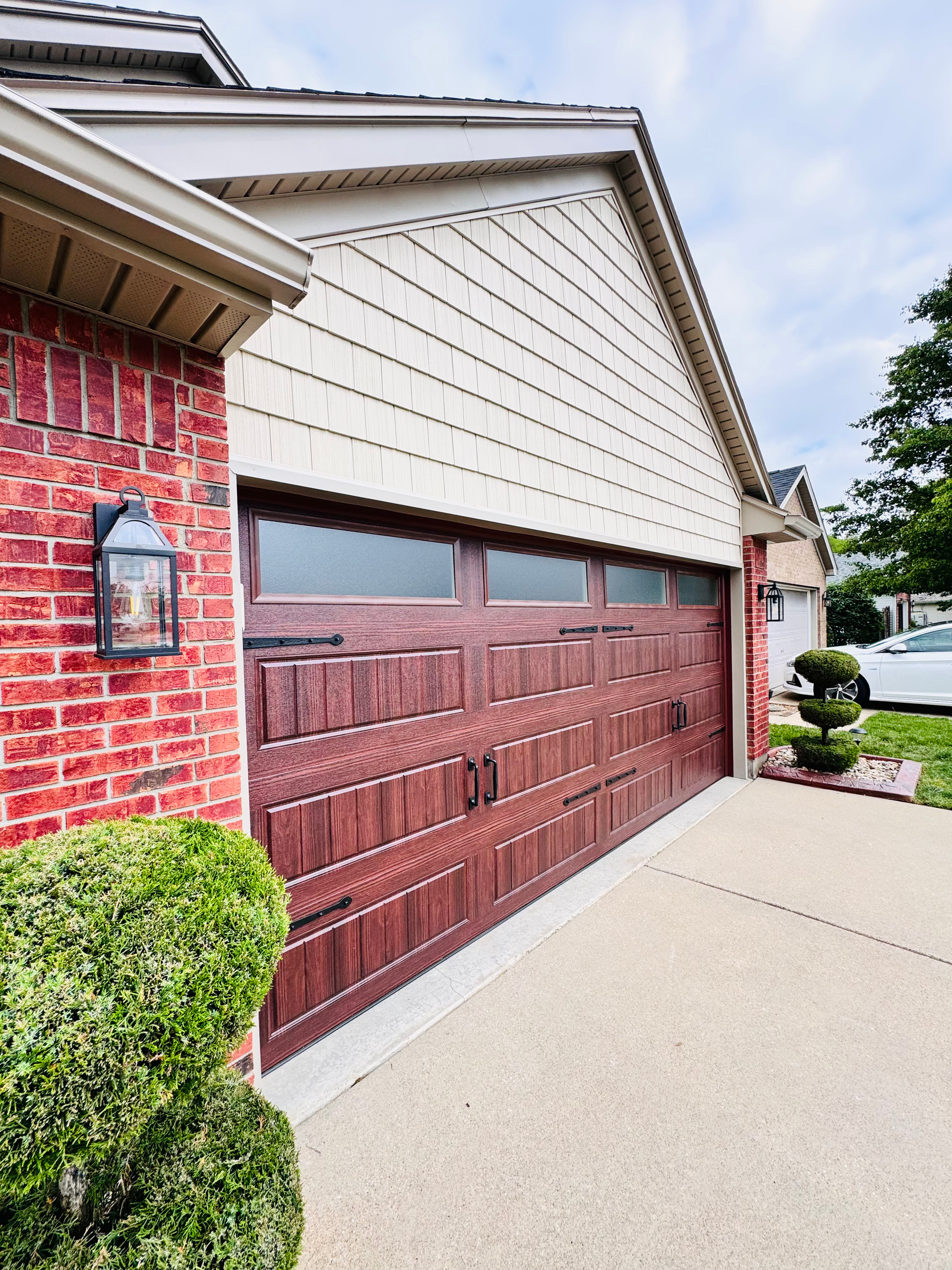 Suburban garage with brown door, red brick wall, and beige siding beside a concrete driveway.