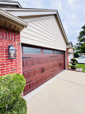 Suburban garage with brown door, red brick wall, and beige siding beside a concrete driveway.