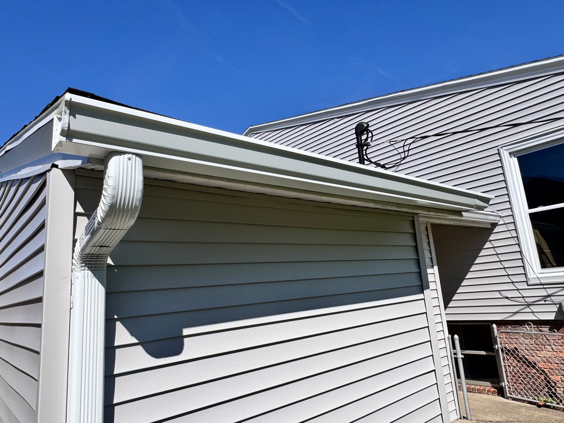 White house gutter and downspout under a gabled roof against a blue sky