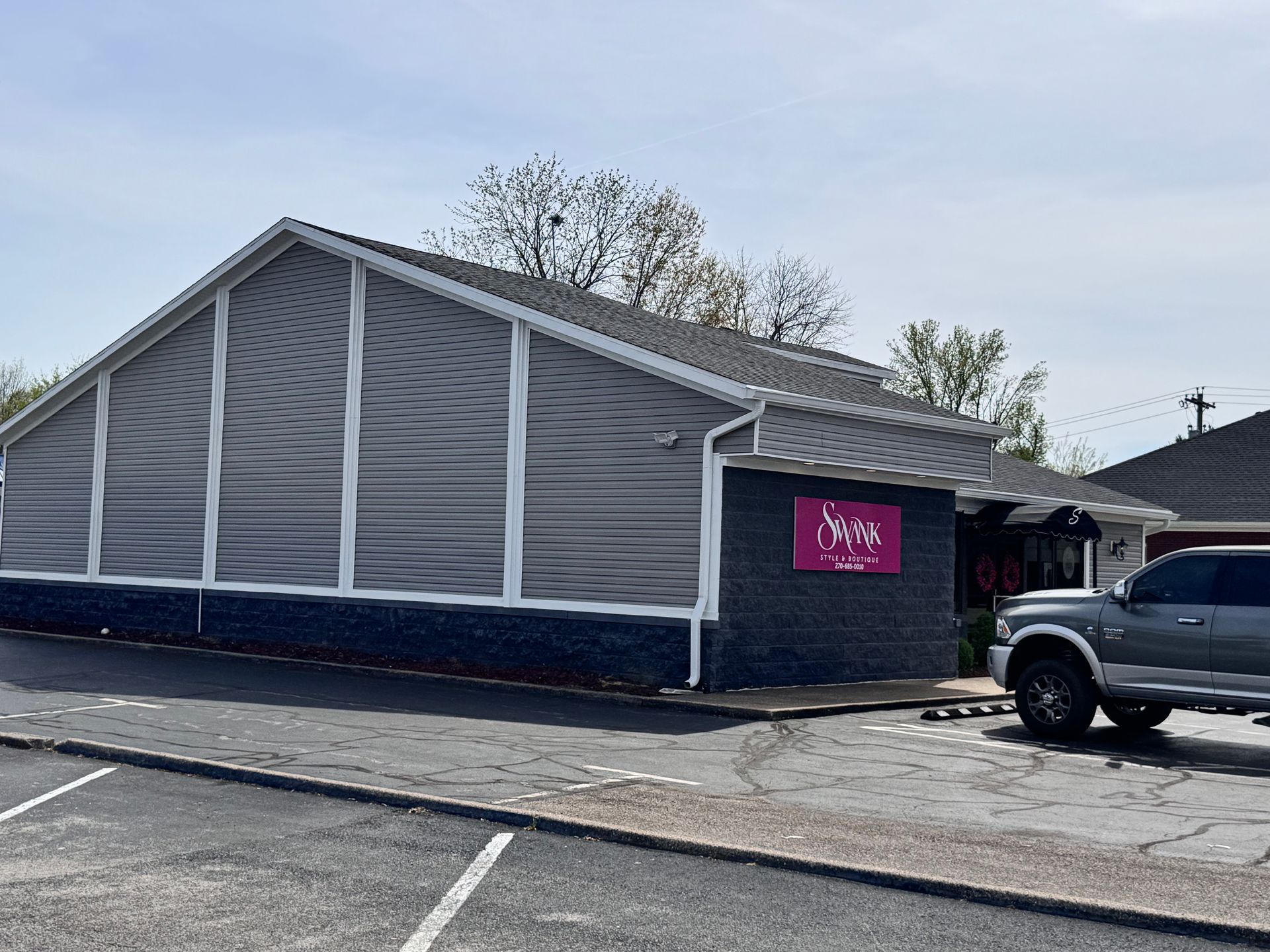 Gray-sided building with a pink sign and a parked black truck in front under a clear sky