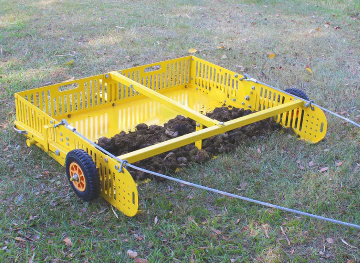 A yellow cart filled with dirt is sitting on the grass