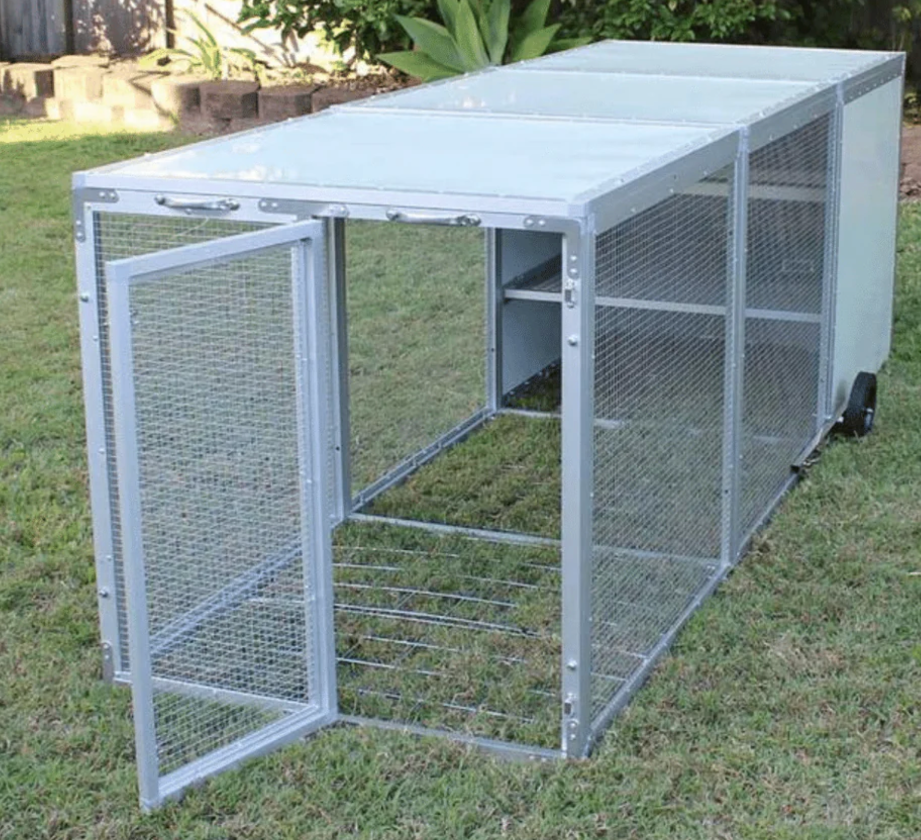 A metal cage is sitting in the grass with the door open