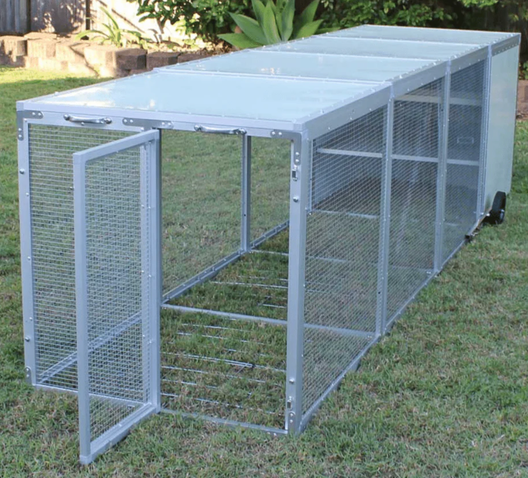 A metal cage is sitting in the grass with the door open