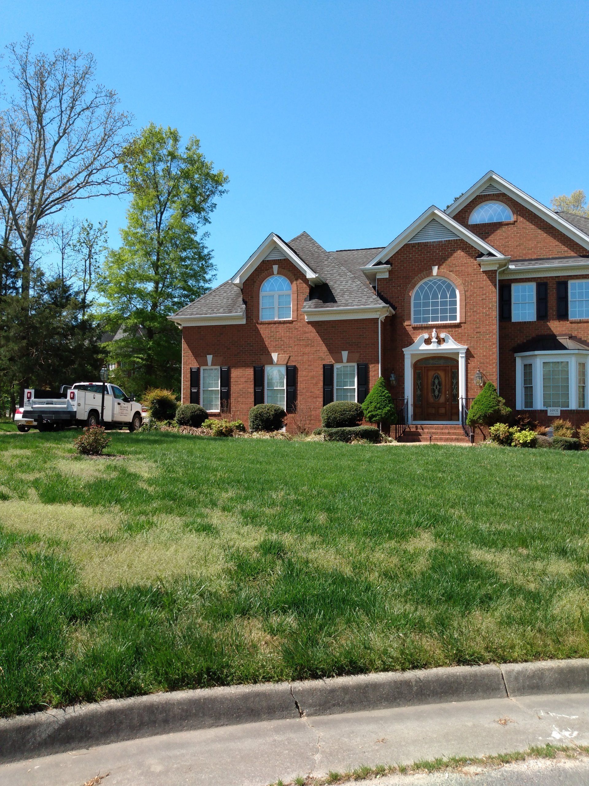 Brick house with a green lawn, blue sky, and a white truck parked to the left.
